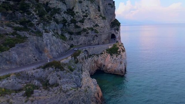aerial shot. Travel by the sea. Serpentine asphalt road under the cliff. Tourism. Stone Cave of counterfeiters in Capo Noli in Liguria, Italy 19.08.2025