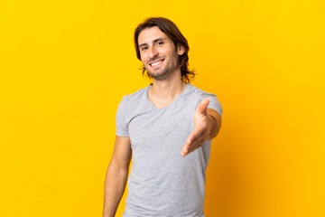 Young handsome man isolated on yellow background shaking hands for closing a good deal