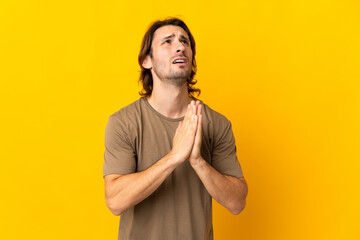 Young handsome man isolated on yellow background keeps palm together. Person asks for something