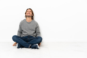 Young handsome man sitting on the floor over isolated background laughing