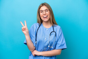 Young surgeon doctor woman isolated on blue background smiling and showing victory sign