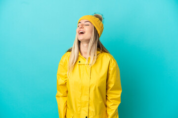 Young woman wearing a rainproof coat over isolated blue background laughing