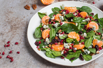 An appetizing festive salad of fresh spinach, tangerine, pomegranate and pine nuts on a plate. 