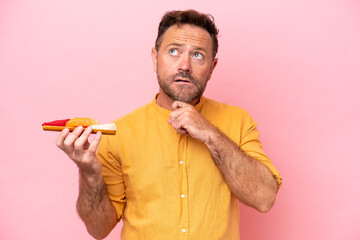 Middle age Caucasian man holding sashimi isolated on pink background and looking up