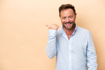 Middle age caucasian man isolated on beige background pointing to the side to present a product