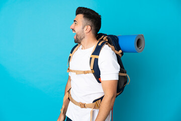 Young mountaineer man over isolated blue background laughing in lateral position