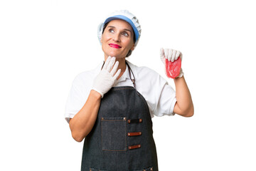 Butcher woman wearing an apron and serving fresh cut meat over isolated background looking up while smiling