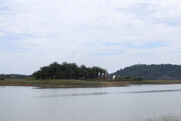Serene lake vista with lush tropical island and distant rolling hills under a cloudy sky