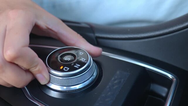 Close-up of hand turning gear shift knob in modern car interior. Driver switches transmission in drive mode on automatic gearbox
