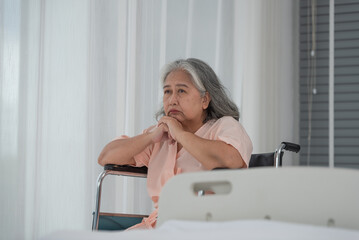 Depressed senior Asian woman patient in hospital sitting in wheelchair by the window, upset disabled patient thinking and looking out window, feeling lonely, nostalgia and melancholy