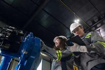 Engineer standing by robotic arm and operating machine in industry factory, technician worker check...