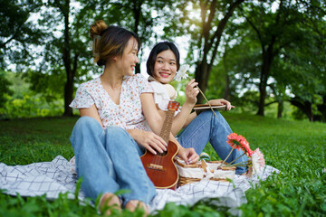 Asian women are joyfully playing guitar and relaxing together under the big tree.