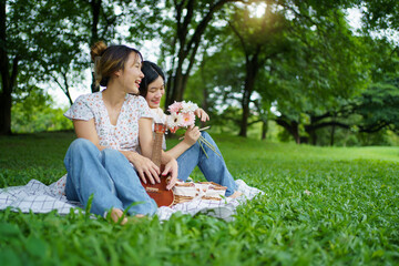 Asian women are joyfully playing guitar and relaxing together under the big tree.