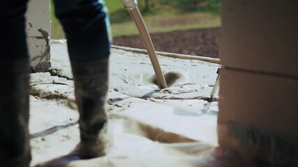 Worker in rubber boots using a concrete poker vibrator to settle wet cement