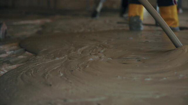 Concrete poker vibrator tool submerged in wet cement screed, removing air bubbles