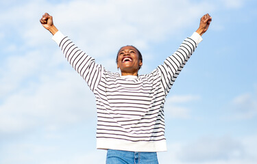 African young woman raising arms with joy under blue sky