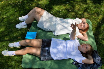 Female students relaxing on a blanket in a park. Summer sunny day