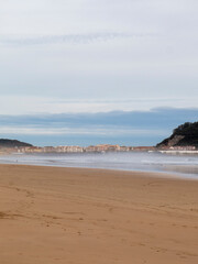 Fototapeta premium Wide sandy beach meeting wavy ocean under cloudy sky in santoña