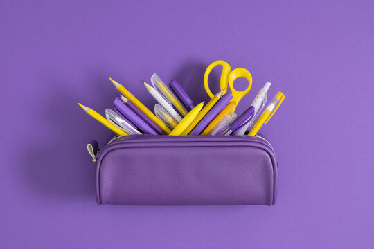 Back to school. Purple full pencil case with pens and pencils on purple background. School educational theme.