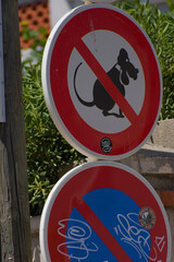 A stack of three circular European-style road signs on a wooden pole, featuring symbols for "no residents", "no rodents", and "no parking with towing", all showing signs of wear and graffiti.