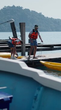 Two young men untying a yellow kayak from the dock before getting into the kayak