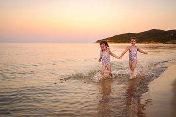 Twin sisters enjoy a joyful run on the shore at sunset