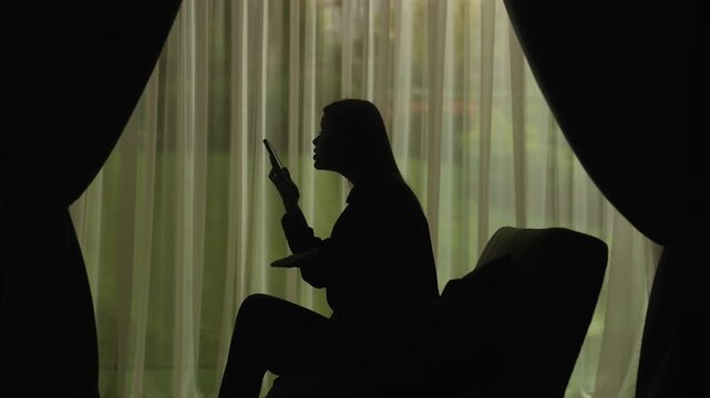 Silhouette of a Person Using Smartphone by Window Curtains