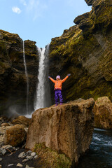 Small cute girl raising her arms up in front of Kvernufoss waterfall in Iceland