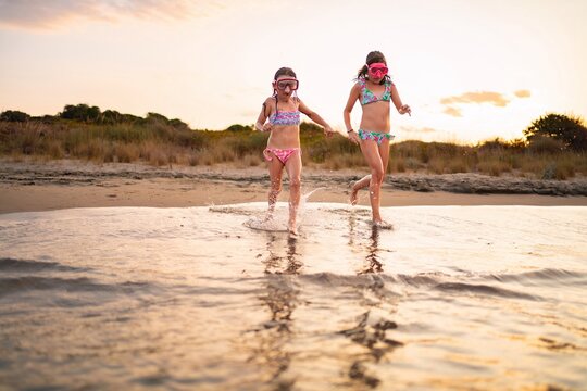 Joyful sisters splashing water during sunset beach adventure