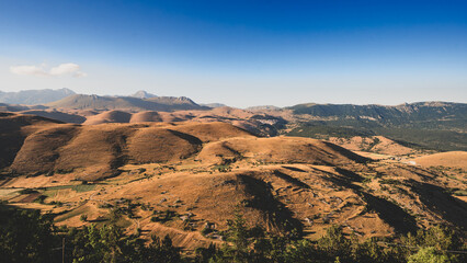 Rolling hills at the foot of Gran Sasso, Abruzzo, Italy, captured at sunset with warm golden light, soft shadows, and a serene landscape blending nature’s curves with mountain majesty.