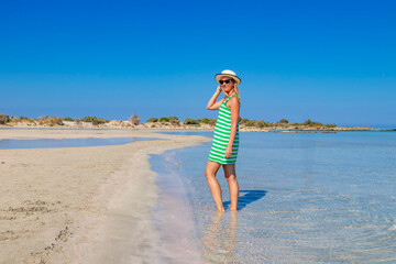 Free happy woman in green striped dress enjoying relaxing beach, joyful in summer by tropical blue water on Elafonisi beach, Greece.