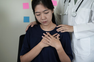 A young asian psychiatrist or healthcare professional woman doctor is gently holding patient, who has a heart disease, hand comforting and encouraging, reassuring woman. Mental health care support.
