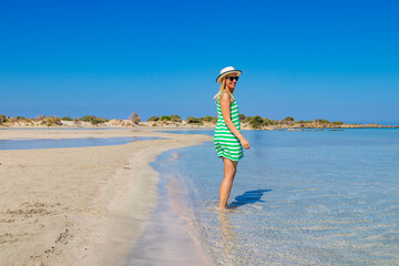 Free happy woman in green striped dress enjoying relaxing beach, joyful in summer by tropical blue water on Elafonisi beach, Greece.