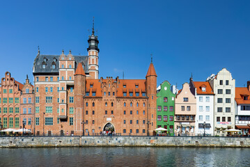 Obraz premium Motlawa River reflects Gdansk architectural spectrum — redbrick history and pastel facades form a vibrant urban collage under clear summer skies. A harbor of color, culture, and memory. Poland