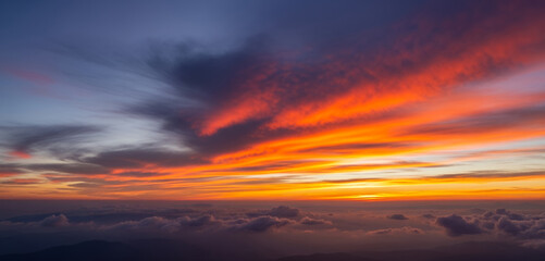 Fototapeta premium Warm rays of light cascade through a vivid sunset sky, painting the mountain peaks with gold and purple tones in a tranquil and atmospheric panorama.
