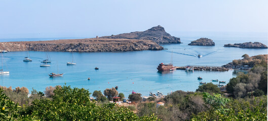 Sailing into serenity &mdash; anchored boats drift in Lindos Bay beneath a sunlit sky, where rocky cliffs meet the calm Mediterranean. A gentle rhythm of coastal life and open horizons.