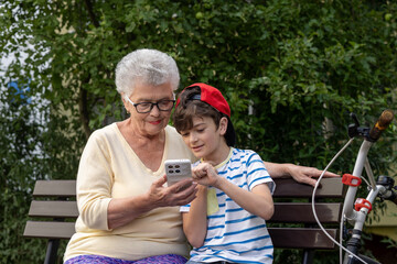Grandmother and Grandson Using Smartphone Together Outdoors. Family connection and technology across generations. Real people, real emotions. Intergenerational Digital Learning. Copyspace