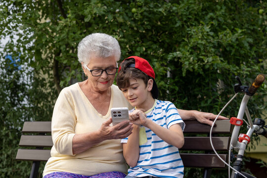 Grandmother and Grandson Using Smartphone Together Outdoors. Family connection and technology across generations. Real people, real emotions. Intergenerational Digital Learning. Copyspace - Powered by Adobe