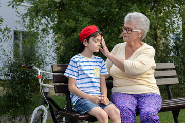 
Caring grandmother checking grandson's temperature and headache in summer park - family health...