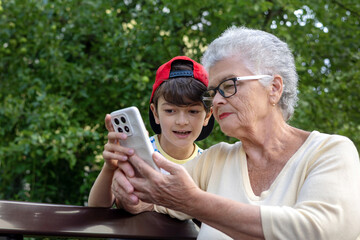 Grandmother and Grandson Using Smartphone Together Outdoors.  Family connection and technology...
