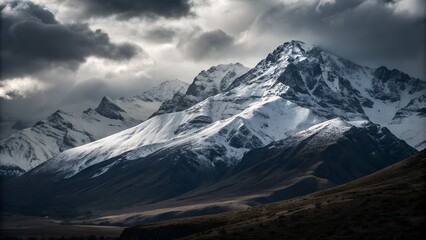 Majestic snow capped mountain peak under dramatic stormy skies with moody clouds and rugged terrain