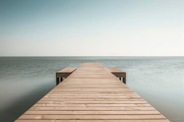 Wooden pier extending into calm ocean under a vast pale sky