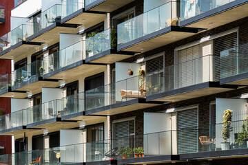 Obraz premium Contemporary glass-balcony apartment block with lush plants and outdoor furniture
