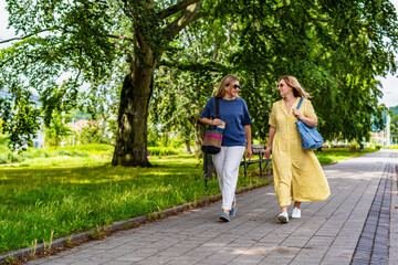 Fototapeta premium Two mature beautiful women walking and talking in city park on summer day 