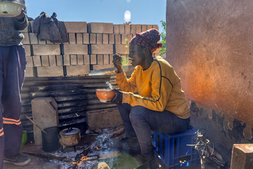Africa village, single woman surrounded by the smoke from the fire cooking soft sorghum porridge,...