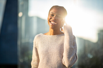 Smiling African American woman enjoying phone chat in golden sunlight