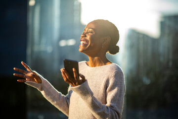 Joyful African American woman gesturing and laughing with phone