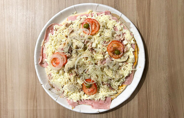 Delicious homemade pizza with ham, mozzarella, tomato, onion, mushrooms, and olives on a wooden table