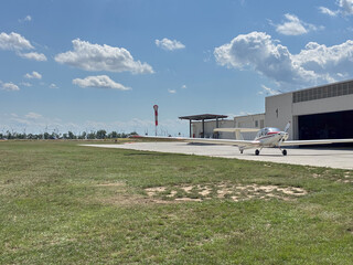 Fototapeta premium A small white and red glider aircraft parked on an airfield with a hangar, windsock, aviation training, and renewable energy integration for flight schools, aerospace industry