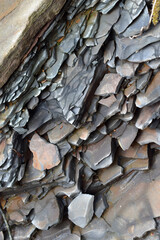 Vertical view of compacted rock layers intersecting at angles revealing geological structure along riverbank where erosion exposes fine sedimentary textures during early spring daylight.